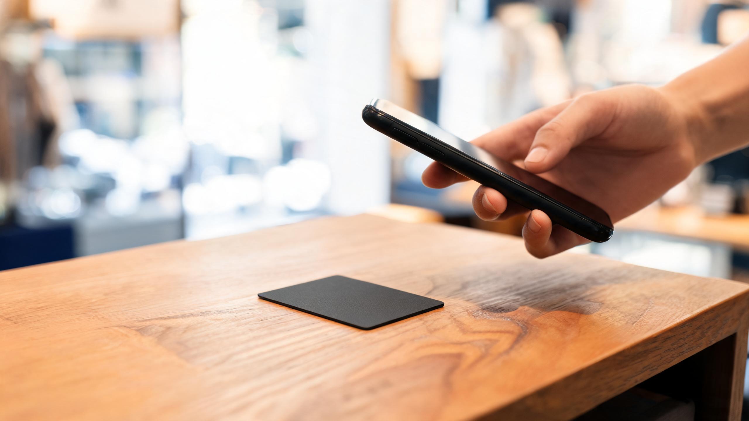 Customer tapping smartphone on NFC card at business counter to leave feedback